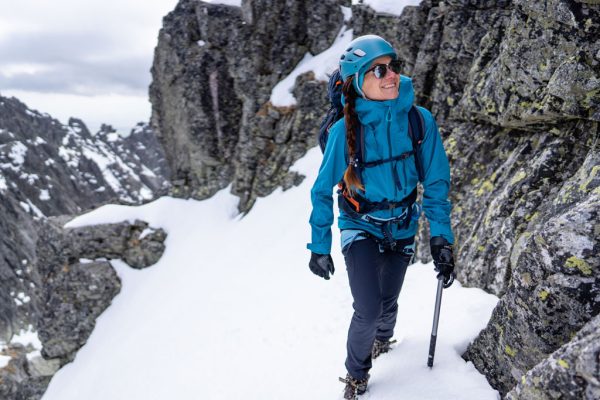 Dámská nepromokavá bunda Rab Firewall Jacket Ultramarine na horolezkyni opírající se o lezecký cepín.
