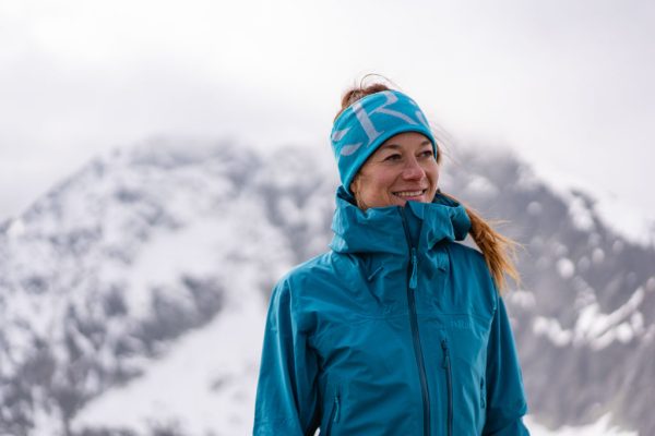 Dámská nepromokavá bunda Rab Firewall Jacket Ultramarine na horolezkyni s modrou čelenkou