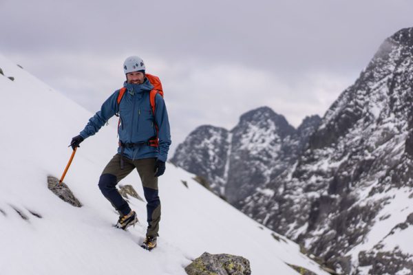 Pánská nepromokavá bunda Rab Firewall jacket Orion Blue na horolezci opírajícím se o horolezecký cepín
