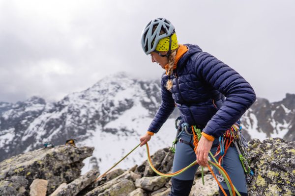 Fialová péřová bunda Rab Mythic Alpine Light pře jištění druholezce ve skalní stěně při provozování horolezectví