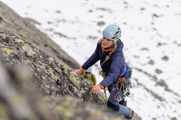 Fialová péřová bunda Rab Mythic Alpine Light pře horolezení ve skalní stěně