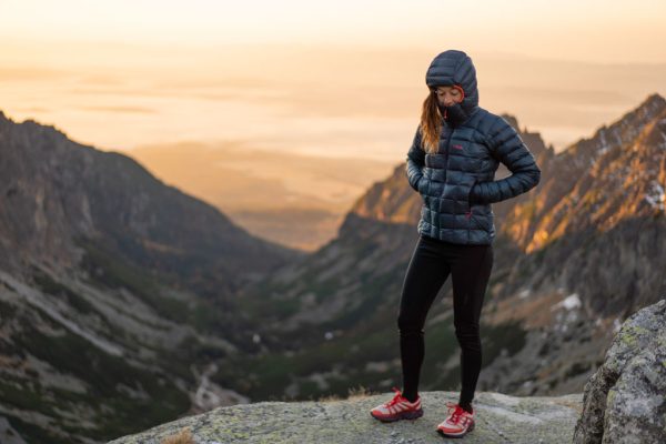 Modrá dámská bunda péřová bunda Rab Mythic Alpine na vrcholku hor při západu slunce