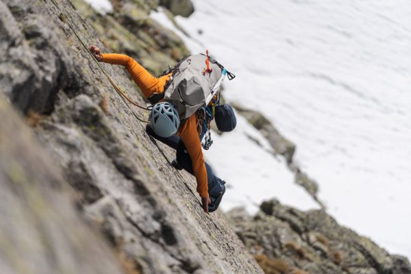 Horolezkyně s helmou a batohem leze po skalní stěně v mikině Rab Ascendor Hoody